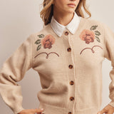 woman wearing an oatmeal button-front cardigan with embroidered rust roses, long puff sleeves and ribbed trim