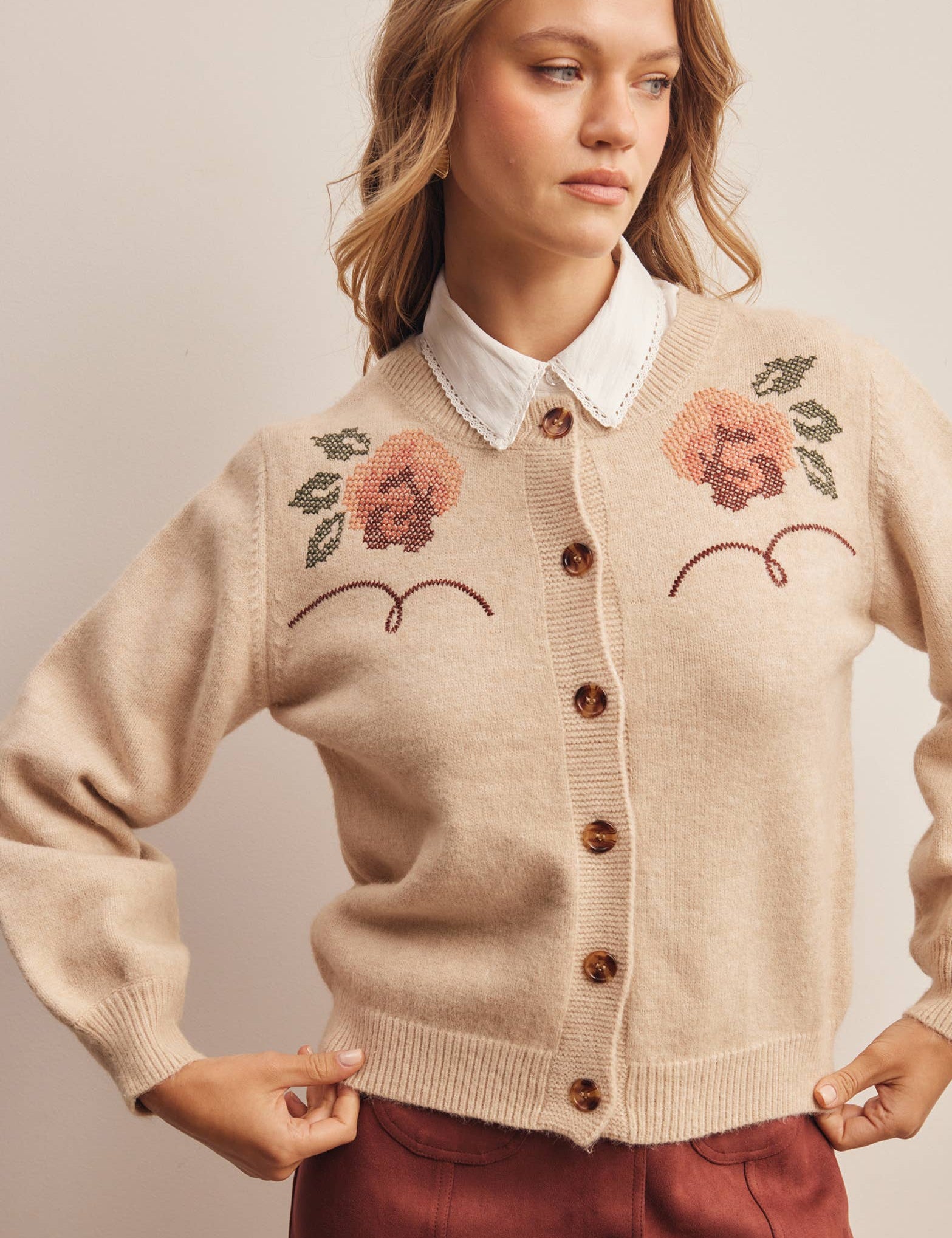 woman wearing an oatmeal button-front cardigan with embroidered rust roses, long puff sleeves and ribbed trim