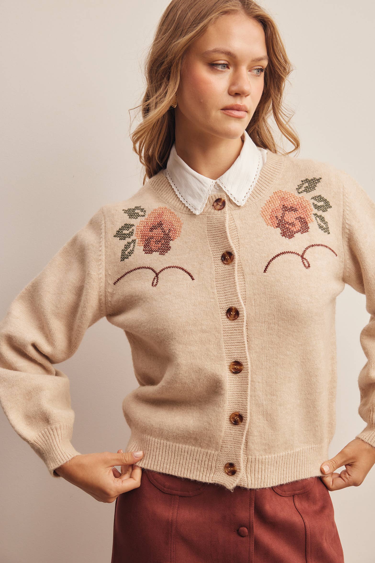 woman wearing an oatmeal button-front cardigan with embroidered rust roses, long puff sleeves and ribbed trim