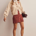 woman wearing an oatmeal button-front cardigan with embroidered rust roses, long puff sleeves and ribbed trim
