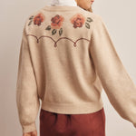 woman wearing an oatmeal button-front cardigan with embroidered rust roses, long puff sleeves and ribbed trim