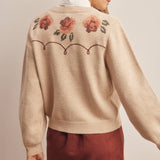 woman wearing an oatmeal button-front cardigan with embroidered rust roses, long puff sleeves and ribbed trim