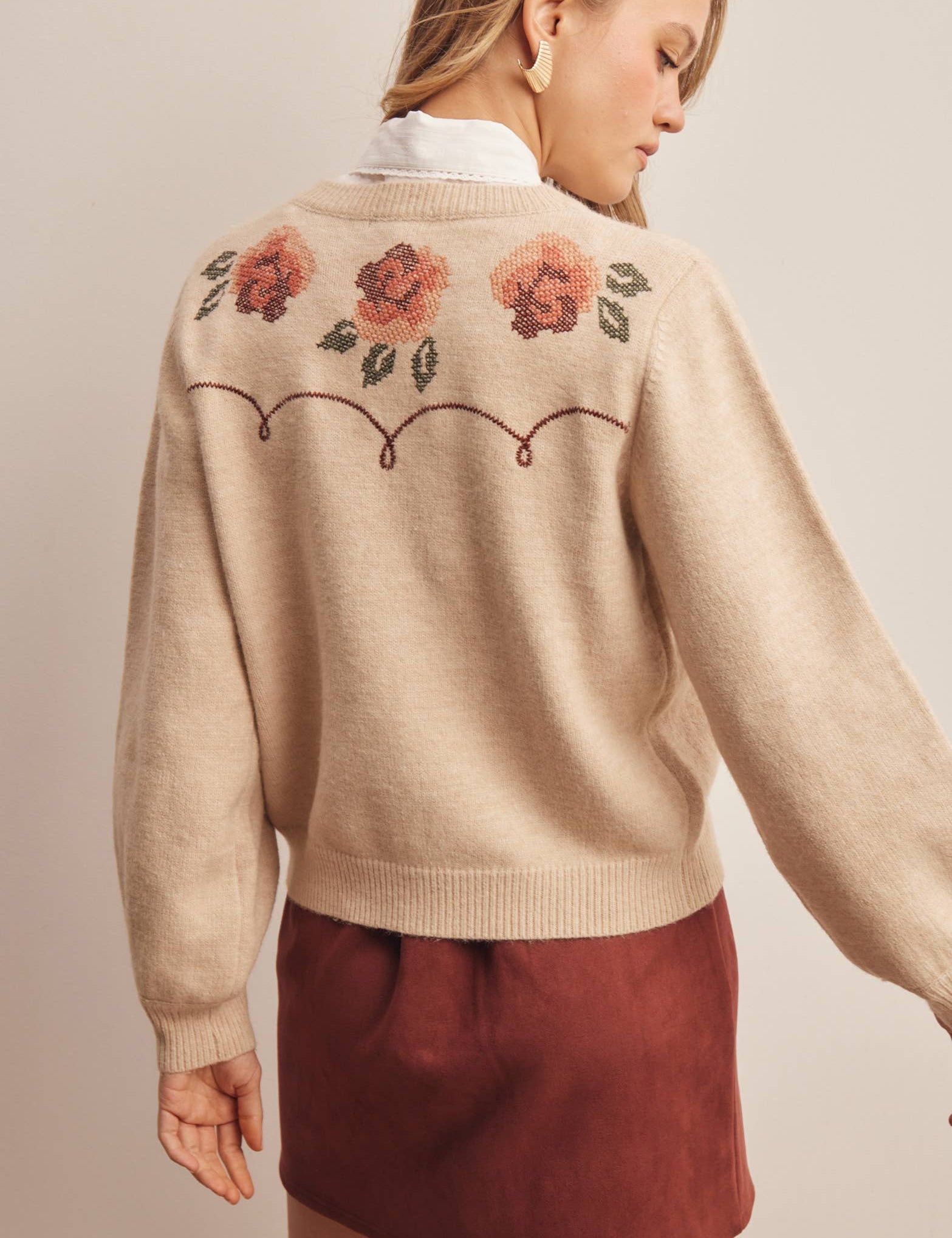 woman wearing an oatmeal button-front cardigan with embroidered rust roses, long puff sleeves and ribbed trim