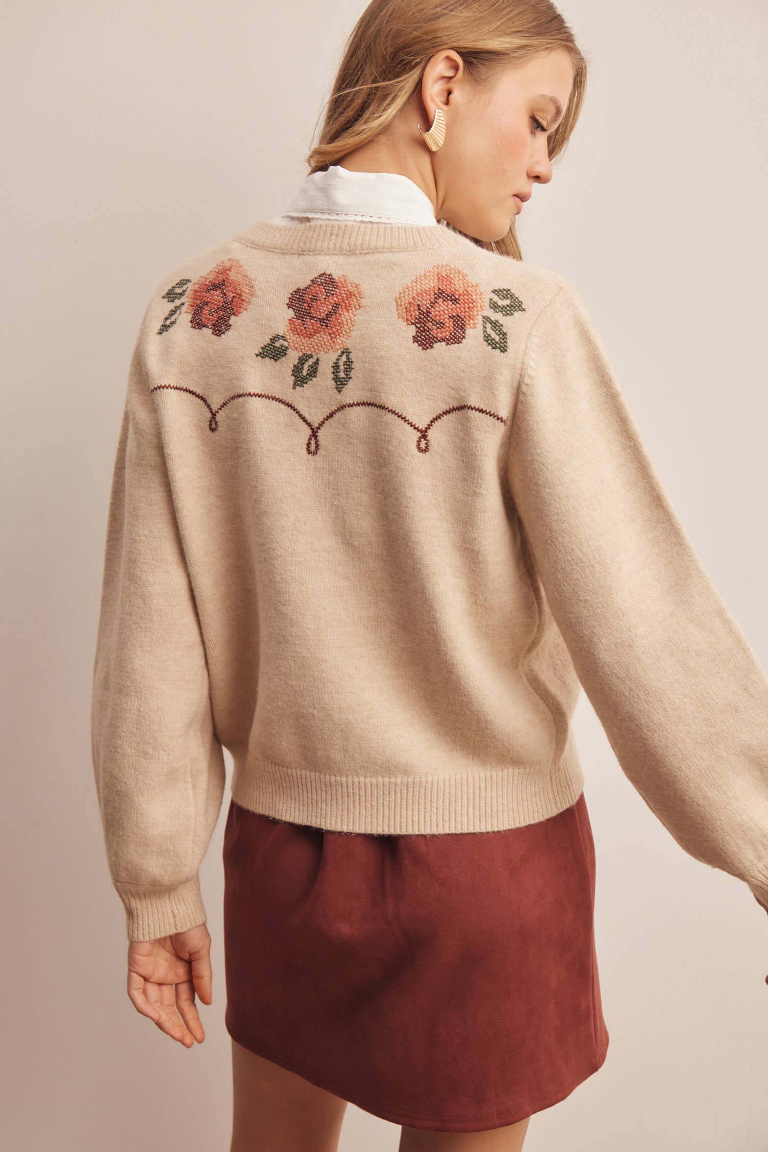woman wearing an oatmeal button-front cardigan with embroidered rust roses, long puff sleeves and ribbed trim