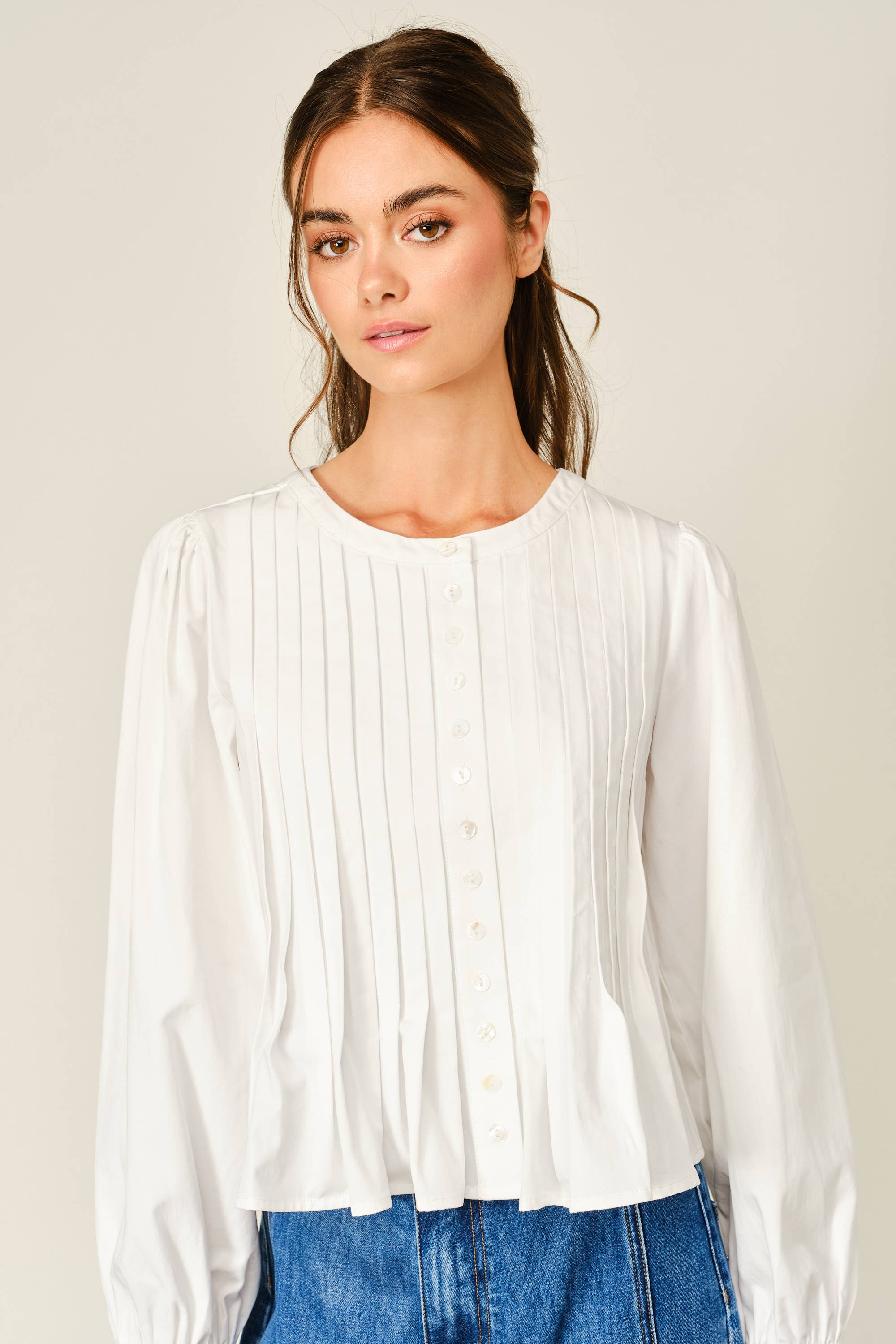 women's white button front blouse with pintuck pleats, long puff sleeves, round neckline, and ruffled babydoll hem