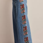 medium wash high rise wide leg jeans with rust and green floral embroidery along the side seams