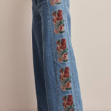 medium wash high rise wide leg jeans with rust and green floral embroidery along the side seams