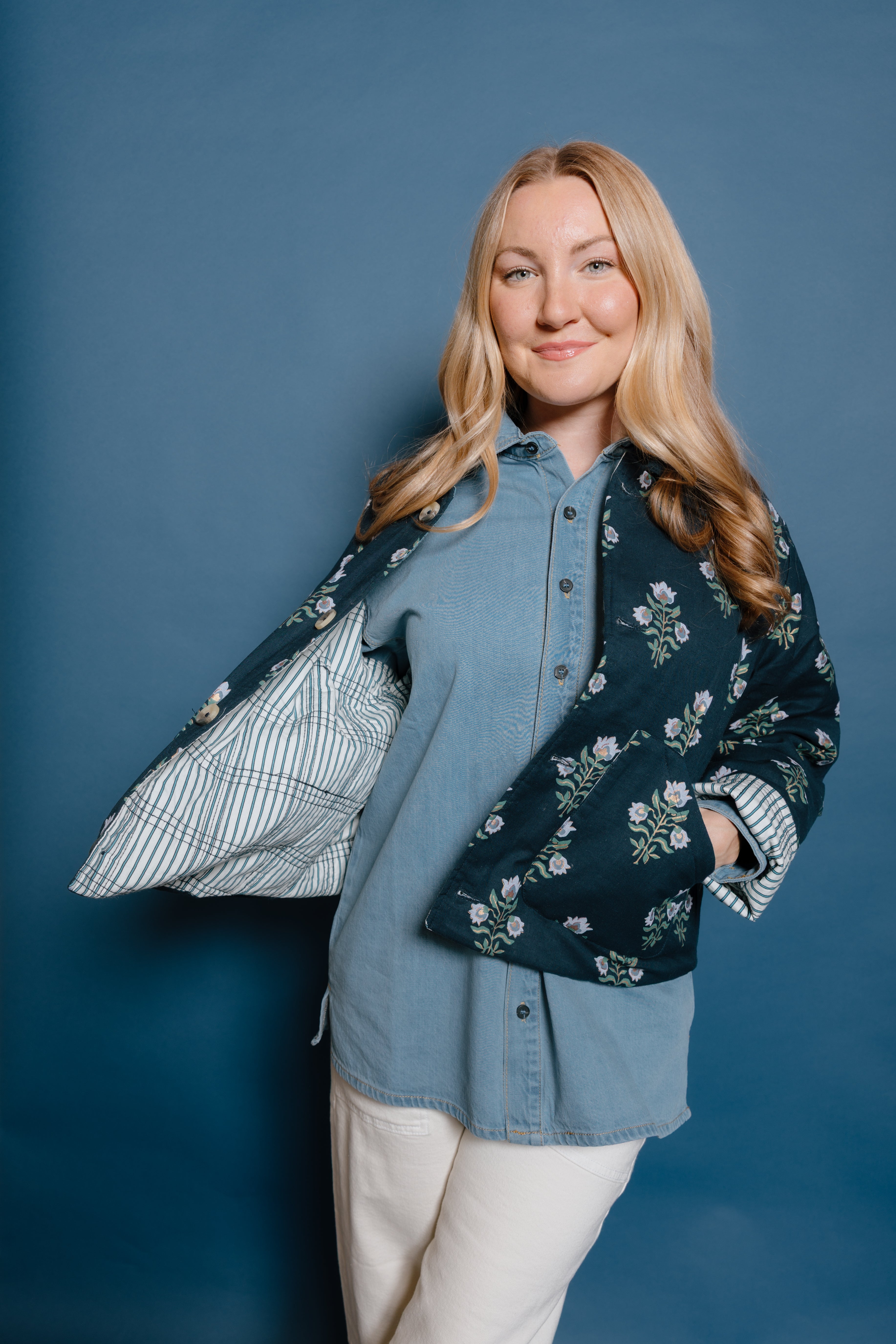 Woman wearing a floral jacket over a denim shirt against a blue background